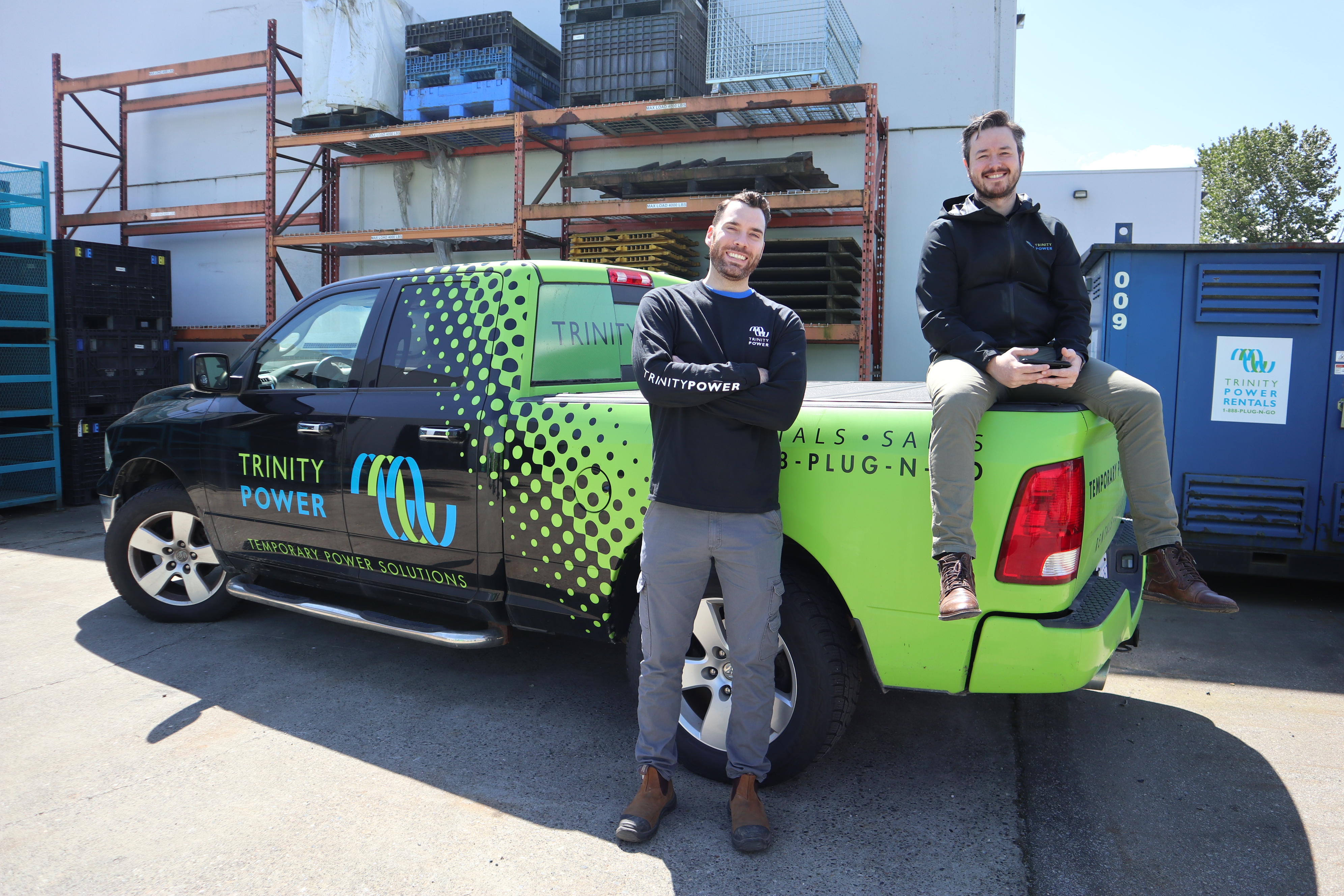 Two Men Are Standing Next To A Trinity Power Truck